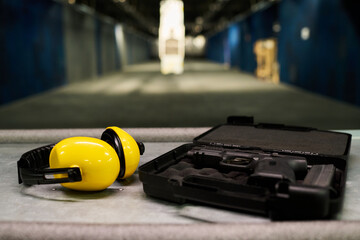 Shot of protective ear muffs and handgun placed on table inside shooting range. Background displays blurred targets and safety equipment