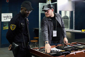 Security professionals discussing in control room with various equipment placed on table. One man demonstrating security gear while another observing and listening attentively