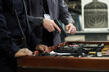 People at shooting range inspecting handgun and arranging equipment on table. Handgun being...