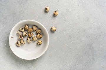 Top view of fresh quail eggs in bowl with soft gray background
