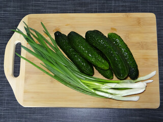 Fresh organic cucumbers and green onions on a rustic wooden cutting board, healthy ingredients for salad, farm-to-table cooking