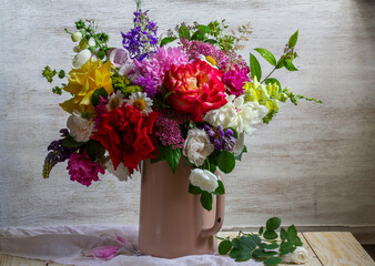 A bouquet of different flowers, roses, peonies, lupines, daisies, dilphinium, snapdragon and others in an old teapot.