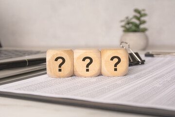 wooden cubes with question marks on financial papers, concept of uncertainty