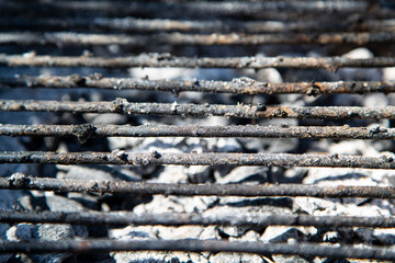 Close-up of a rustic used barbecue grill with burnt charcoal beneath metal bars, ideal for illustrating outdoor cooking, summer grilling, camping lifestyle, or backyard barbecue themes...