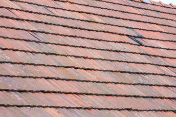 Detailed view of old terracotta roof tiles with some visible damage and a dark patch, showing wear,