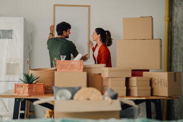 Couple hanging picture frame in new home while unpacking boxes
