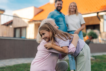 Fototapeta premium Granddaughter hugging grandmother in front of house with family watching