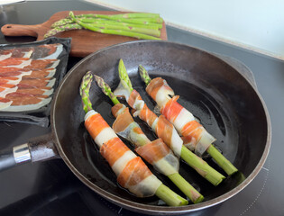 Asparagus wrapped in prosciutto and cheese frying in a cast iron pan – homemade appetizer...