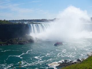 Niagara Falls. A pleasure boat with people near the huge famous waterfall. View from the Canadian side. Nature scenery. Photo for advertising, background, wallpaper, postcards.
