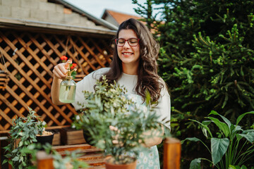 Young woman taking care of plants with water can and mister	