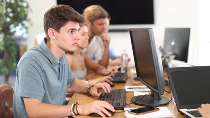 Concentrated interested junior software developer working in IT startup, sitting at computer desk and coding with group of coworkers