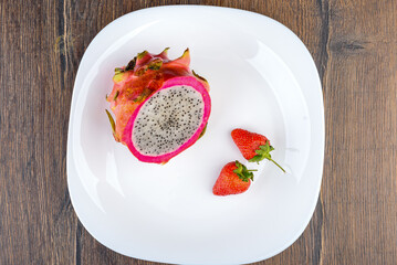 Top view of a white plate with half a pitahaya and two strawberries.