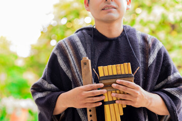 Young Andean Indian man, dressed in traditional poncho with Andean wind instruments.