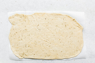 Overhead view of rolled out crackers dough on parchment paper, cracker biscuit dough on white background, process of making crackers