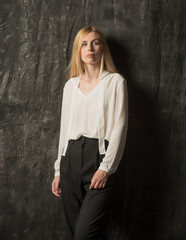 Fototapeta premium portrait of a blonde woman with long hair in black pants and a white shirt. young woman posing on a dark background