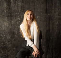 Naklejka premium portrait of a blonde woman with long hair in black pants and a white shirt. young woman posing on a dark background