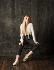 Naklejka premium portrait of a blonde woman with long hair in black pants and a white shirt. young woman posing on a dark background