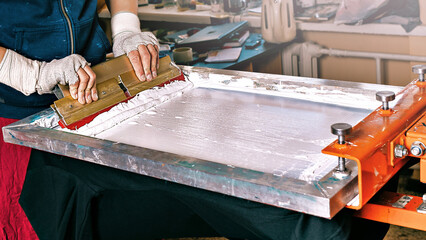 silk screen textile printery. manual screen printing. selective focus photo of male hands with a squeegee