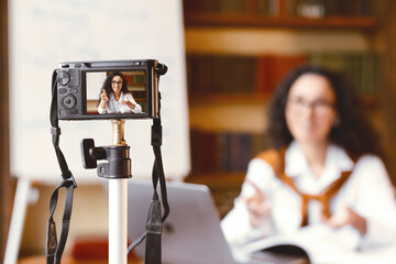 People And Technology Concept. Young woman in glasses sitting at desk, recording broadcast at home,...