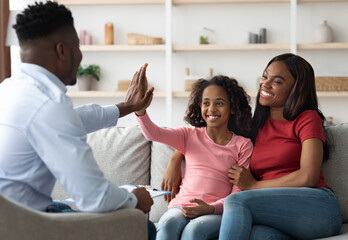 Positive black mother and daughter teenager at the appointment with male psychologist, happy african american girl giving psychotherapist high five, clinic interior, family therapy session concept