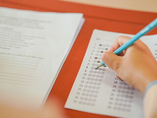 Obraz premium Closeup of female student's hand doing exam in classroom. School proficiency test. Asian student doing exam. Education, learning