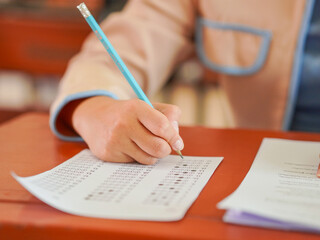 Closeup of female student's hand doing exam in classroom. School proficiency test. Asian student...