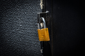 Detail of a yellow padlock closing a black gate with a wrinkled wall in Brazil