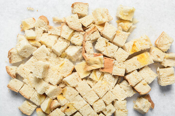 Overhead view of bread being sliced into cubes on a white countertop, process of making bread pudding