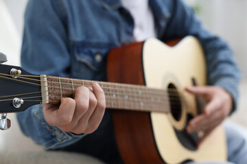 Man playing guitar on armchair indoors, closeup