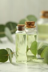 Bottles of essential oil and eucalyptus leaves on white marble table, closeup