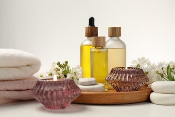 Spa products, burning candles, pebble stones and twigs with beautiful flowers on white table, closeup
