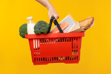 Man holding shopping basket with different products on yellow background, closeup