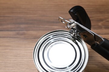 Can opener and tin on wooden table, closeup. Space for text