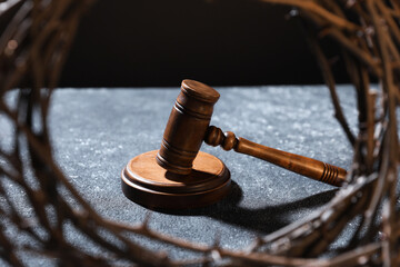 View of judge's gavel through crown of thorns on dark textured table