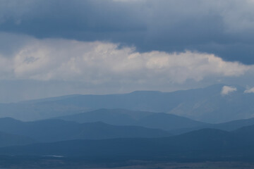 Obraz premium Lines of mountains on the horizon, gradually fading into soft blue tones under a cloudy sky