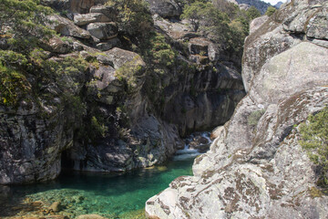 Emerald-colored mountain stream in a granite canyon under a clear blue sky, crystal clear water, rocky landscape