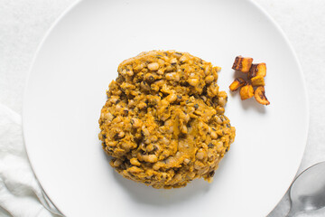 Overhead view of nigerian fried beans and fried plantain on a white plate, top view of nigerian stewed beans and plantain on a white background