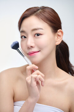 Young Asian Woman Applying Makeup with Brush on White Background