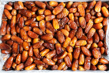 An overhead shot showcases a dense arrangement of Medjool dates, their glossy surfaces reflecting light. The rich brown and amber tones create a visually appealing texture ideal for culinary.