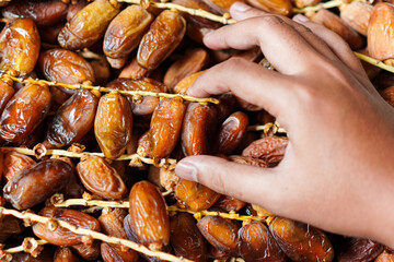 Close-up shows a hand selecting naturally sun-dried dates still on their stems, highlighting the organic texture and rich color of these sweet, healthy treats in a bountiful display.