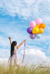 Vertical Cheerful cute girl holding balloons running on green meadow white cloud blue sky with...