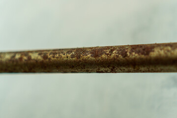 Close-up shot capturing the texture of a metal rod. The rod displays a weathered surface. Rust and corrosion patterns evoke a sense of age and decay against the blurred neutral background.