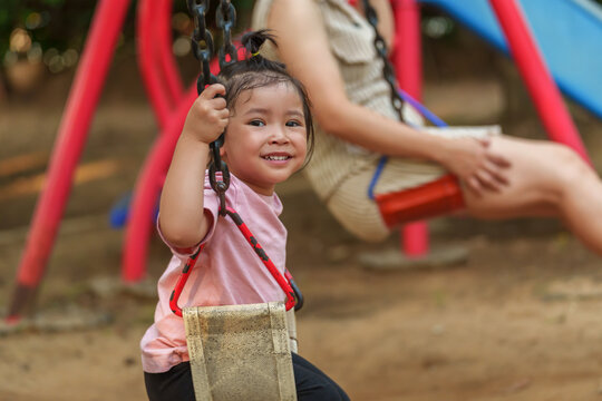 cheerful toddler girl with mother playing on a swing at playground