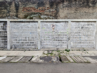 Weathered brick wall beneath a textured surface contrasts with a block wall, adorned by a faded...