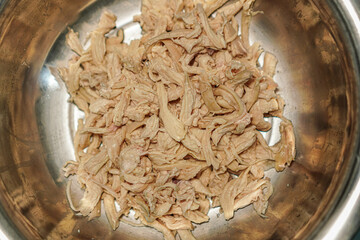 Overhead view of shredded cooked poultry in a stainless steel bowl, ideal for illustrating healthy...