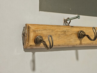 Close-up of a rustic wooden rack with aged, coiled metal hooks mounted on a clean white wall. The...