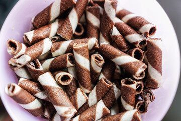 An enticing high-angle close-up shot presents a delightful heap of brown and white striped wafer rolls. The arrangement invites the eye to linger on the tasty, inviting snacks.