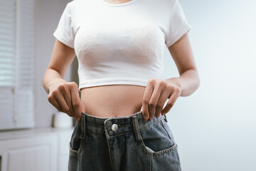Young woman proudly showing loose jeans, symbolizing successful weight loss and fitness...