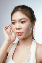 A young Asian woman with clear skin gently touches her face, showcasing natural beauty, skincare routine, and a healthy lifestyle.
