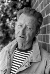 Fototapeta premium Senior man posing near brick wall in monochrome analog film photography